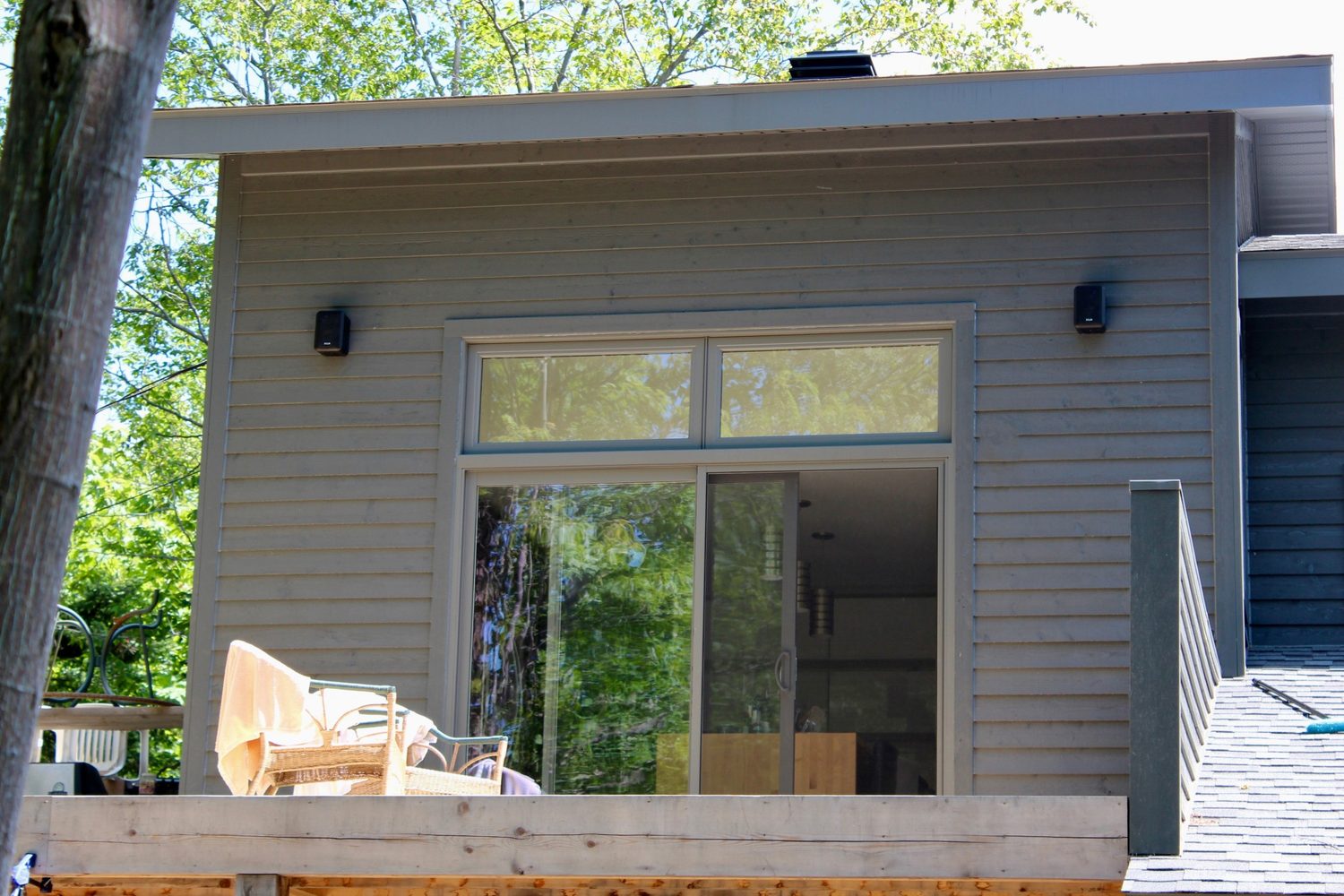 Une maison moderne au déclin gris, fenêtres charbon, porte-patio ouverte sur une galerie de bois